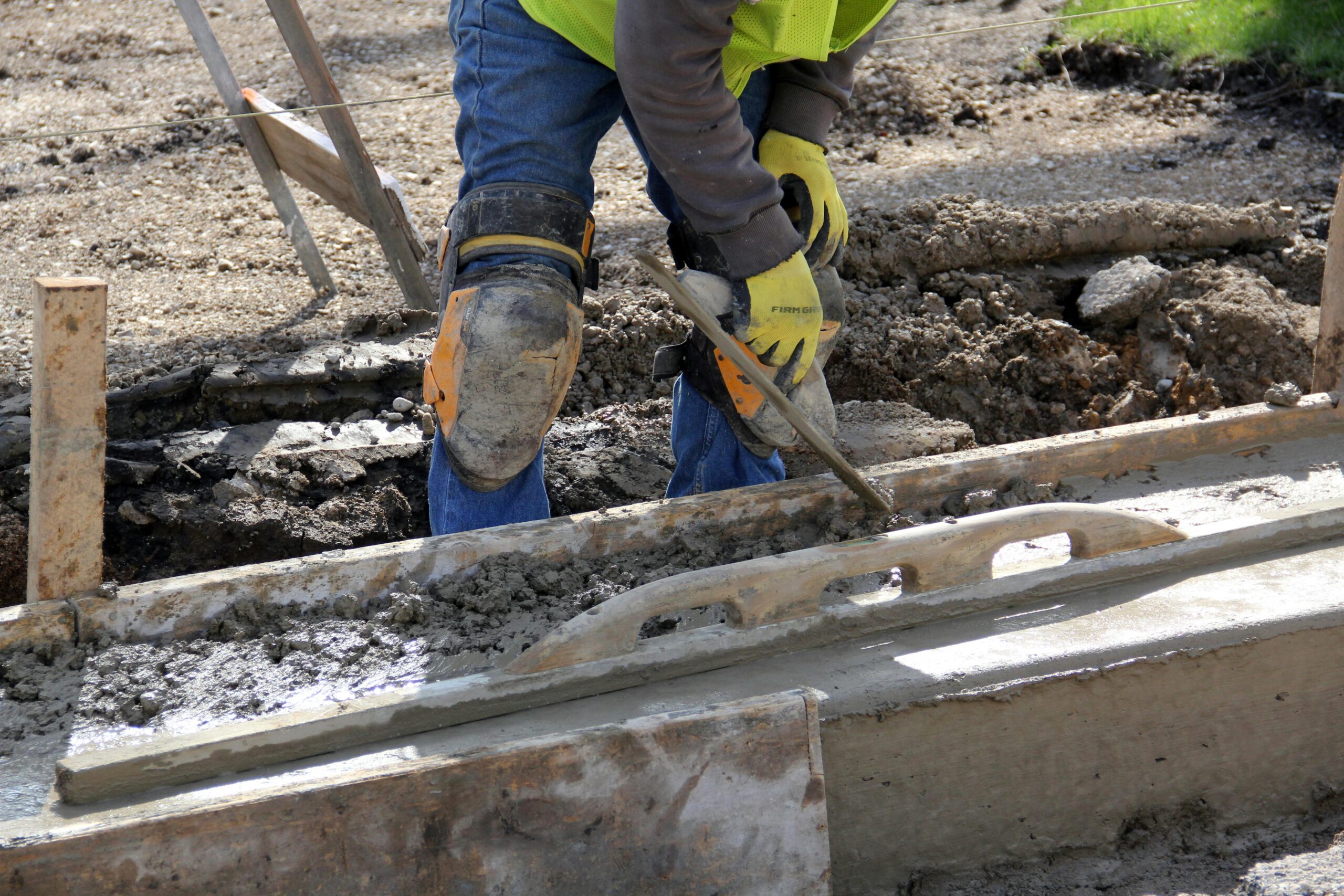 Worker using a trowel to smooth concrete at an outdoor construction site.